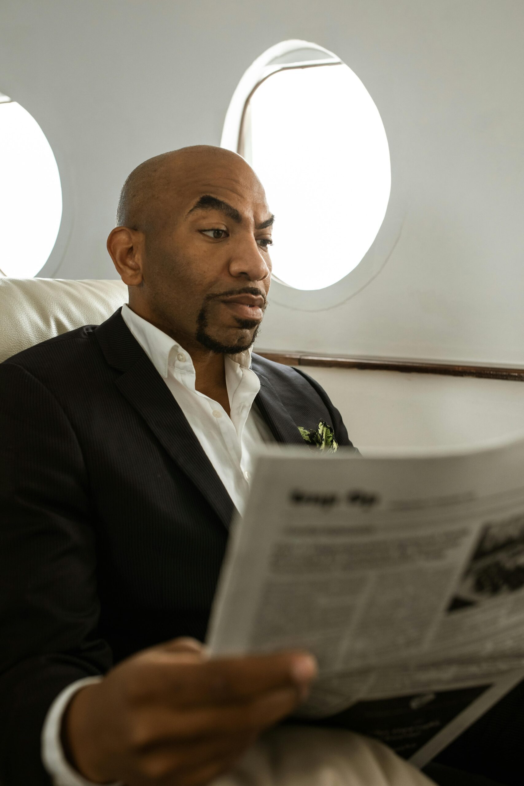 African American man in suit reading newspaper in private jet. Focused and relaxed.