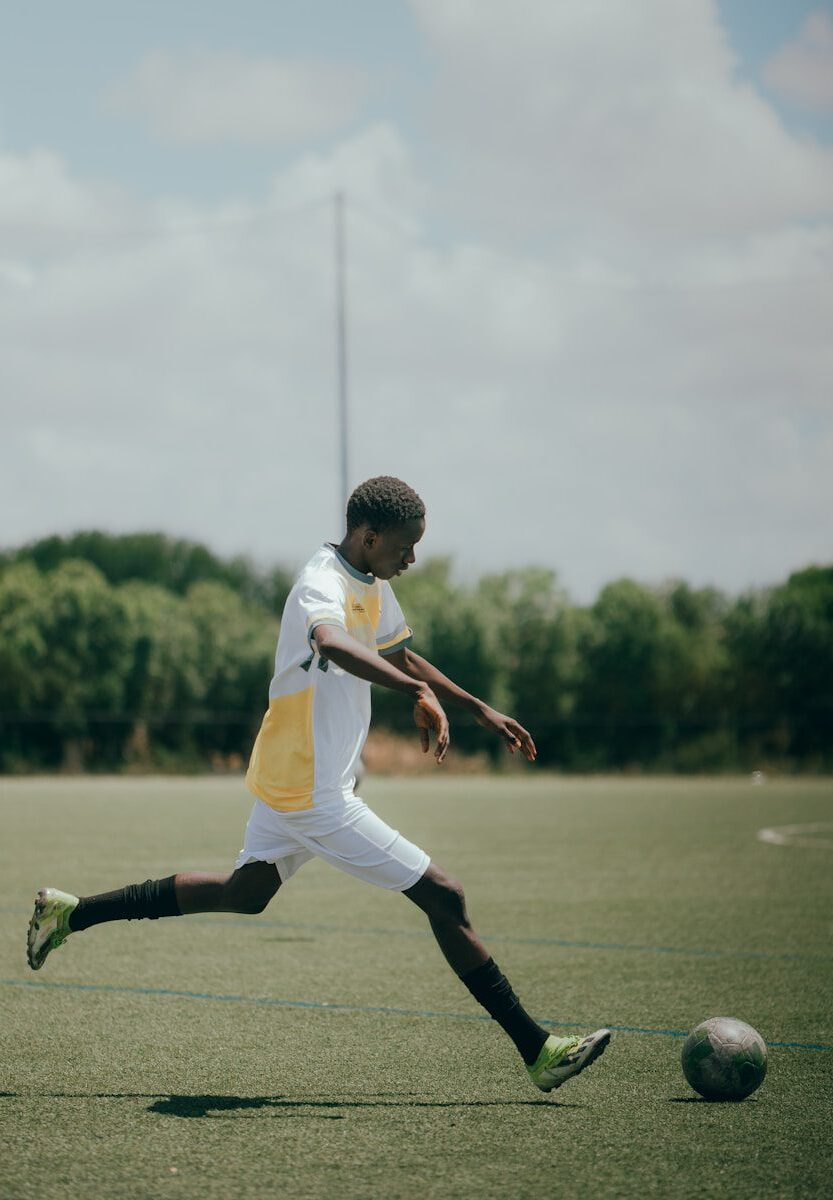 Soccer player kicks the ball on a green field.